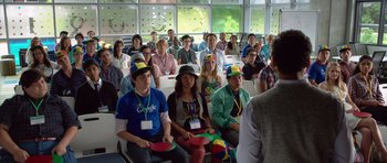 Movie still from “The Internship” (2013), directed by Shawn Levy – A group of people sitting in front of an audience wearing hats; Medium shot, Over the shoulder angle
