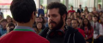 Movie still from “The Internship” (2013), directed by Shawn Levy – A man with a beard wearing headphones in front of a group of people; Close Up shot, Over the shoulder angle