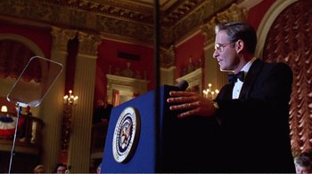 Movie still from “Dave” (1993), directed by Ivan Reitman – A man standing at a podium in front of a microphone; Medium shot, Low angle