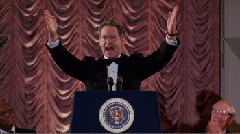 Movie still from “Dave” (1993), directed by Ivan Reitman – A man standing at a podium raising his hands in the air; Medium shot, Low angle