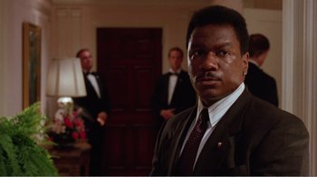 Movie still from “Dave” (1993), directed by Ivan Reitman – A man wearing a suit and tie in front of two other men; Close Up shot, Low angle