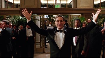 Movie still from “Dave” (1993), directed by Ivan Reitman – A man in a tuxedo waving at the camera; Medium shot, Low angle