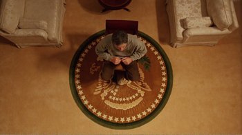 Movie still from “Dave” (1993), directed by Ivan Reitman – A man sitting on the floor of a living room; Wide shot, Overhead angle