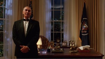 Movie still from “Dave” (1993), directed by Ivan Reitman – A man standing in front of a desk in front of a window; Medium shot, Low angle