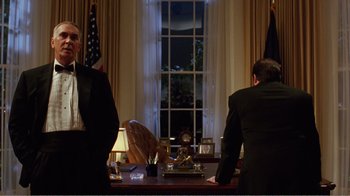Movie still from “Dave” (1993), directed by Ivan Reitman – Two men in suits are sitting at a desk in front of a window; Medium shot, Low angle