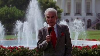 Movie still from “Dave” (1993), directed by Ivan Reitman – An older man wearing a suit and tie while holding a microphone; Medium shot, Low angle