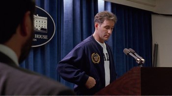 Movie still from “Dave” (1993), directed by Ivan Reitman – A man standing in front of a microphone in front of a podium; Medium shot, Over the shoulder angle