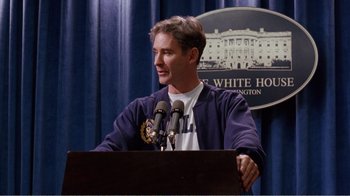 Movie still from “Dave” (1993), directed by Ivan Reitman – A man standing at a podium with microphones; Medium shot, Low angle