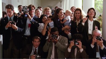 Movie still from “Dave” (1993), directed by Ivan Reitman – A group of people taking a picture with a camera; Wide shot, High angle
