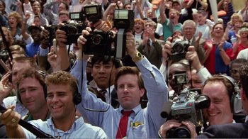 Movie still from “Dave” (1993), directed by Ivan Reitman – A group of people holding up cameras in front of a crowd of onlookers; Medium shot, High angle