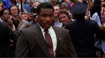 Movie still from “Dave” (1993), directed by Ivan Reitman – A man in a suit and tie with headphones on his ears; Close Up shot, Low angle