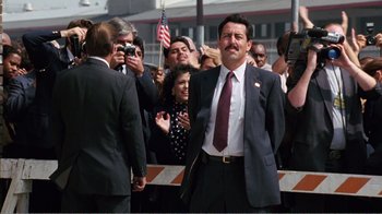Movie still from “Dave” (1993), directed by Ivan Reitman – A man in a suit and tie standing in front of a group of onlookers; Medium shot, Low angle