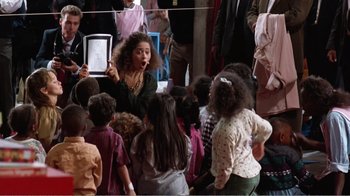 Movie still from “Dave” (1993), directed by Ivan Reitman – A group of children standing in a room with a woman; Medium shot, High angle