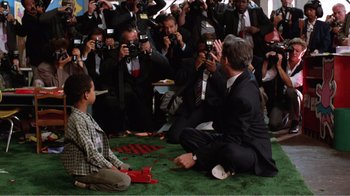 Movie still from “Dave” (1993), directed by Ivan Reitman – A group of people taking pictures of a man sitting on the ground; Wide shot, High angle