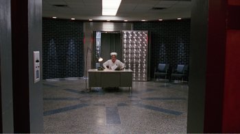 Movie still from “Dave” (1993), directed by Ivan Reitman – A man sitting at a desk in a room; Wide shot, High angle