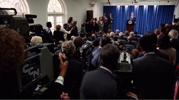 Movie still from “Dave” (1993), directed by Ivan Reitman – A crowd of people watching a man speak at a press conference; Wide shot, High angle