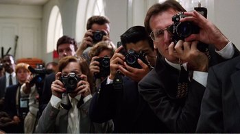 Movie still from “Dave” (1993), directed by Ivan Reitman – A group of people taking pictures with cameras; Medium shot, Low angle