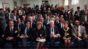 Movie still from “Dave” (1993), directed by Ivan Reitman – A group of people sitting in a room with papers in their hands; Wide shot, High angle