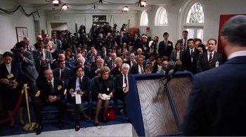 Movie still from “Dave” (1993), directed by Ivan Reitman – A group of people sitting in front of microphones in a room; Wide shot, High angle
