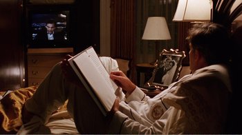 Movie still from “Dave” (1993), directed by Ivan Reitman – A person sitting on a bed holding a book; Medium shot, Over the shoulder angle