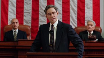 Movie still from “Dave” (1993), directed by Ivan Reitman – A man standing at a podium in front of an american flag; Medium shot, Low angle