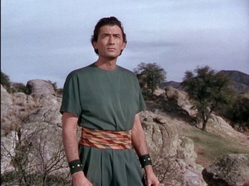 Movie still from “David and Bathsheba” (1951), directed by Henry King – A man in a green shirt and a brown belt standing in front of rocks; Medium shot, Low angle