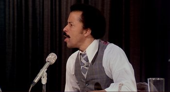 Movie still from “Dawn of the Dead” (1978), directed by George A. Romero – A man in a vest and tie is speaking into a microphone; Close Up shot, Low angle