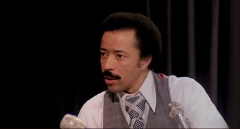 Movie still from “Dawn of the Dead” (1978), directed by George A. Romero – A man with a beard and a mustache wearing a vest and a tie; Close Up shot, High angle