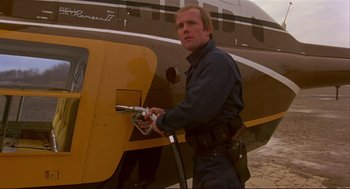 Movie still from “Dawn of the Dead” (1978), directed by George A. Romero – A man pumping gas into a yellow and black airplane; Medium shot, Over the shoulder angle