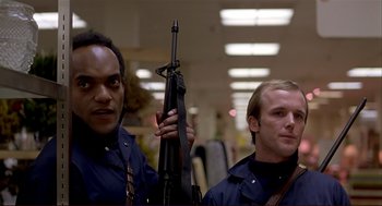 Movie still from “Dawn of the Dead” (1978), directed by George A. Romero – Two men holding a rifle in a room with lights; Medium shot, Low angle
