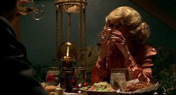 Movie still from “Dawn of the Dead” (1978), directed by George A. Romero – A woman sitting at a dinner table drinking from a wine glass; Medium shot, Over the shoulder angle
