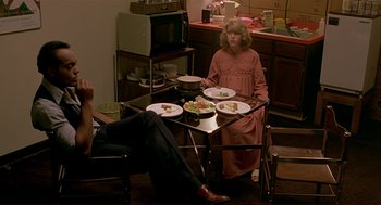 Movie still from “Dawn of the Dead” (1978), directed by George A. Romero – A woman sitting at a table with a plate of food on top of it; Wide shot, High angle