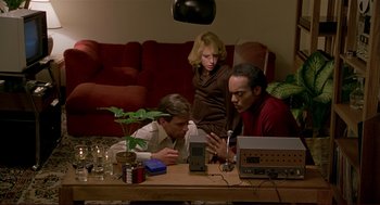 Movie still from “Dawn of the Dead” (1978), directed by George A. Romero – A group of people sitting at a table with electronics; Medium shot, High angle