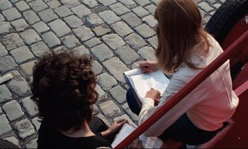 Movie still from “Day for Night” (1973), directed by François Truffaut – Two women sitting on a bench writing on paper; Medium shot, High angle
