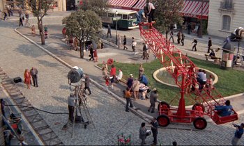 Movie still from “Day for Night” (1973), directed by François Truffaut – A group of people standing on a sidewalk near a fountain; Extreme Wide shot, High angle