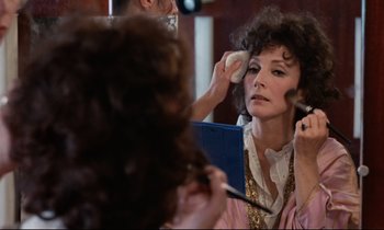 Movie still from “Day for Night” (1973), directed by François Truffaut – A woman putting makeup on her face in front of a mirror; Close Up shot, Over the shoulder angle