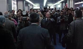 Movie still from “Day for Night” (1973), directed by François Truffaut – A group of people taking pictures of a man in a suit; Wide shot, Over the shoulder angle