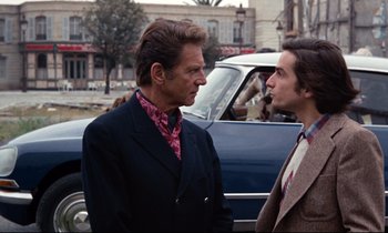 Movie still from “Day for Night” (1973), directed by François Truffaut – A man in a suit talks to another man in front of a car; Medium shot, Over the shoulder angle