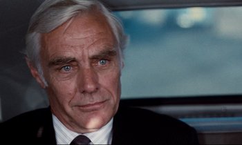 Movie still from “Day for Night” (1973), directed by François Truffaut – An older man in a suit and tie in front of a car; Close Up shot, Over the shoulder angle