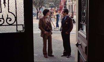 Movie still from “Day for Night” (1973), directed by François Truffaut – Two men standing on the sidewalk talking to each other; Wide shot, Over the shoulder angle