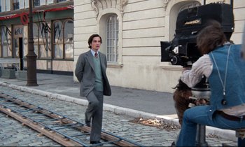 Movie still from “Day for Night” (1973), directed by François Truffaut – A man in a suit and tie standing next to a building; Wide shot, Low angle