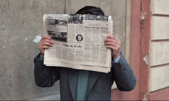 Movie still from “Day for Night” (1973), directed by François Truffaut – A man in a suit and tie holding up a newspaper; Medium shot, High angle