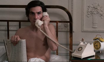 Movie still from “Day for Night” (1973), directed by François Truffaut – A man sitting in a bed holding a phone to his ear; Medium shot, High angle