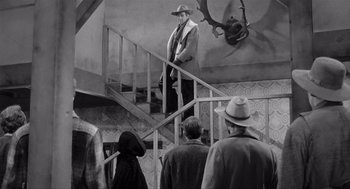 Movie still from “Day of the Outlaw” (1959), directed by André De Toth – A man in a suit and hat standing at the top of a flight of stairs; Wide shot, Low angle