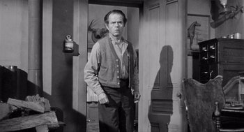 Movie still from “Day of the Outlaw” (1959), directed by André De Toth – A man standing in front of a door in a room; Medium shot, Over the shoulder angle