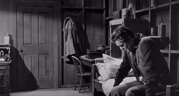 Movie still from “Day of the Outlaw” (1959), directed by André De Toth – A man sitting on a bench in a room; Medium shot, High angle