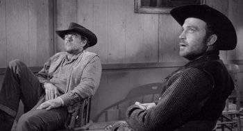 Movie still from “Day of the Outlaw” (1959), directed by André De Toth – Two men sitting in a chair in front of a wooden wall; Medium shot, Over the shoulder angle