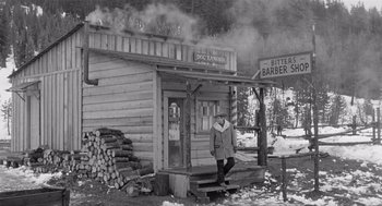 Movie still from “Day of the Outlaw” (1959), directed by André De Toth – An old photo of a man standing outside of a barber shop; Wide shot, High angle