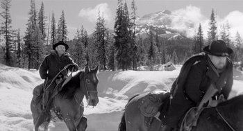 Movie still from “Day of the Outlaw” (1959), directed by André De Toth – A black and white photo of two people riding horses; Wide shot, Low angle