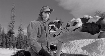 Movie still from “Day of the Outlaw” (1959), directed by André De Toth – A black and white photo of a man holding a snowboard; Medium shot, Low angle